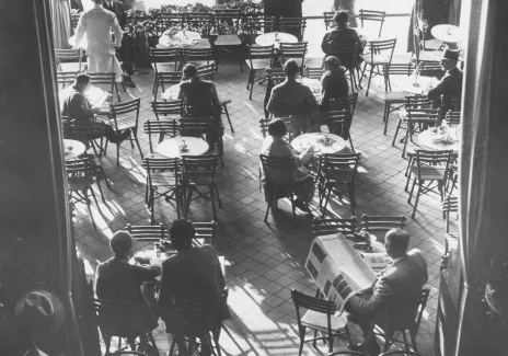 Czarno-biala fotografia kawiarni. Kilka rzędów zajętych stolików.