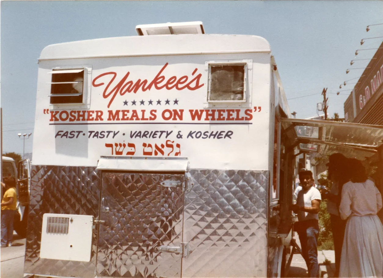 Kolorowa fotografia. Duża furgonetka rozwożąca koszerne jedzenie. Z tyłu napis w języku angielskim: Yankee's Kosher Meals on Wheels, czyli Yankees's koszerne jedzenie na kółkach.