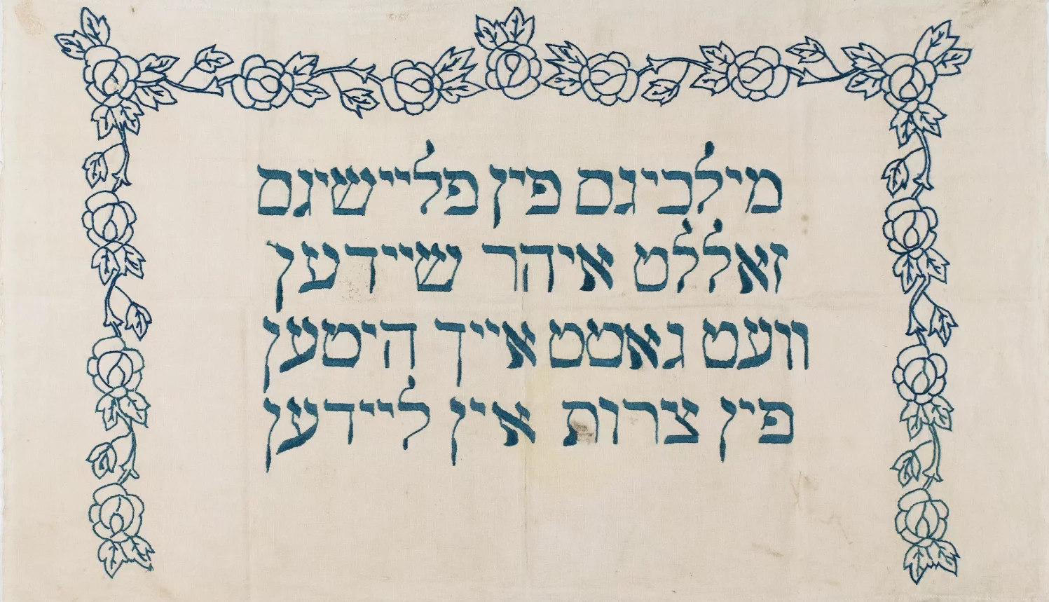 Granatowe litery hebrajskie na jasnym tle. Wokół nich obramowanie w kwiatowych wzorach.