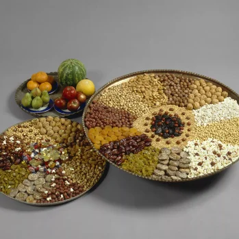 Two large flat dishes filled evenly with fine multi-colored dried fruits. Next to them is a small plate with small round fruits.