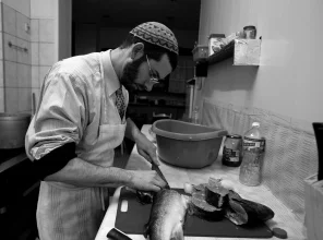 Wnętrze kuchni, przy blacie kuchennym rabin kroi na duże kawałki rybę
