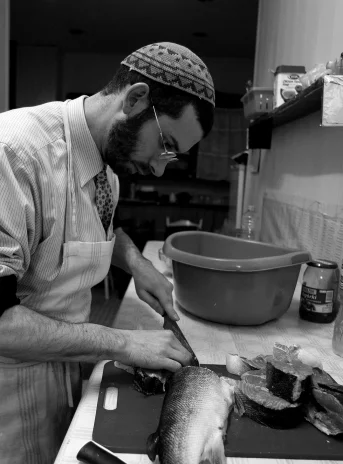 The interior of the kitchen, at the kitchen counter the rabbi cuts fish into large pieces