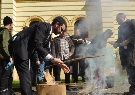 A group of men stands in front of the building. One of them leans over a small bonfire lit on the sidewalk.