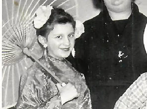 Dwoje dzieci i kobiea w średnim wieku pozują do zdjęcia. Dziewczynka w stroju japońskim, chłopiec w stroju kowbojskim. Kobieta w długiej czarnej sukni i kapeluszu.