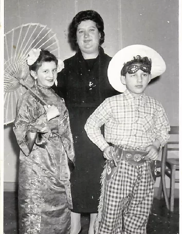 Dwoje dzieci i kobiea w średnim wieku pozują do zdjęcia. Dziewczynka w stroju japońskim, chłopiec w stroju kowbojskim. Kobieta w długiej czarnej sukni i kapeluszu.