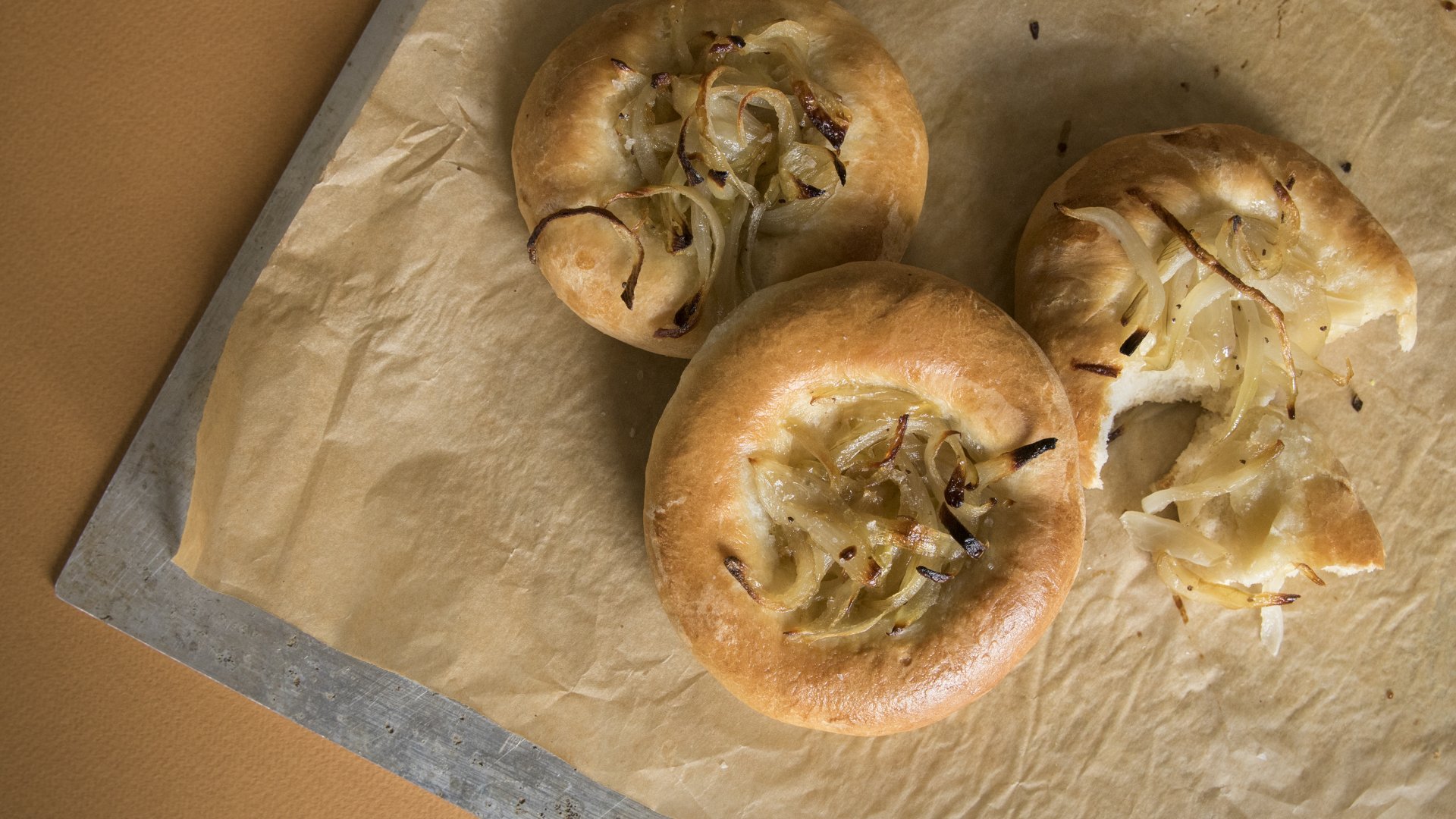 Na papierze do pieczenia ułożone są trzy bułeczki bialystoker kuchen. Jedna z nich jest przygryziona.